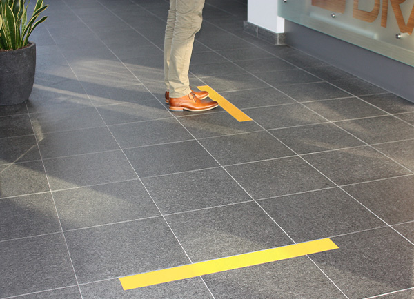 Vinil kompozit karodan elleriyle ToughStripe Vinil zemin bandını söken bir kişi. Bant tek parça halinde temiz bir şekilde sökülüyor.