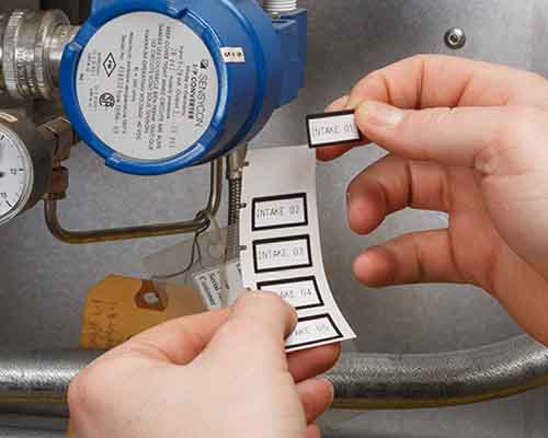 Bir kişi, M610 ile yazdırılmış etiketleri bir makineye uyguluyor.