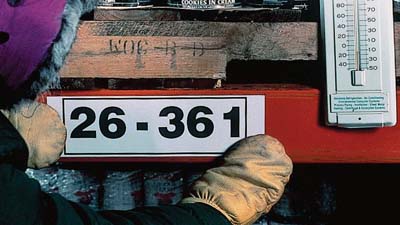 Tek parmaklı eldiven giyen bir kişi, dondurucunun içine bir etiket uyguluyor.