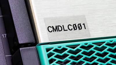 Bir elektronik ekipman parçasının paslanmaz çeliğine uygulanmış Brady ultra-kuvvetli yapışkanlı şeffaf polyester etiket.