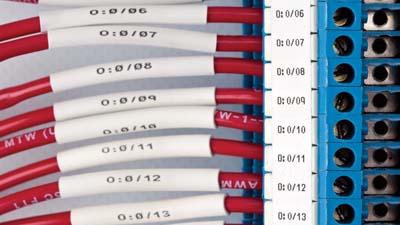 Terminal bloğunun içindeki ısıyla daralan tanımlama makaronlarına sahip bir dizi kırmızı kablo.