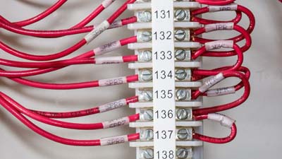 Beyaz bir terminal bloğu etiketi ile tanımlanmış, terminal bloğu içindeki bir dizi kırmızı tel.