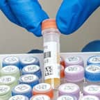 İki barkod etiketine sahip bir test tüpünü tutan laboratuvar teknisyeni.