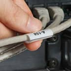 Gri bir kabloya sarılabilir etiket uygulayan bir kişi.