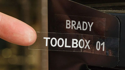 Bir metal parçasına yapıştırılmış, beyaz yazıyla “Brady toolbox 01” yazan şeffaf bir etiket.