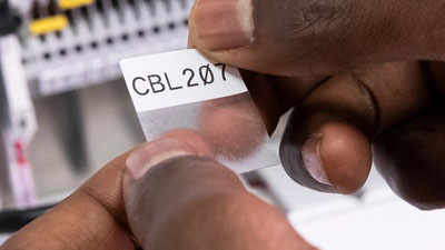 Brady’nin güçlü yapışkanlı kendinden laminasyonlu vinil etiketini bir tel veya kabloya uygulamak üzere olan bir teknisyen. Metin, beyaz etiket bölümüne net bir şekilde basılmıştır ve uygulandığında metni saracak ve kaplayacak şeffaf bir bölüm bulunur.