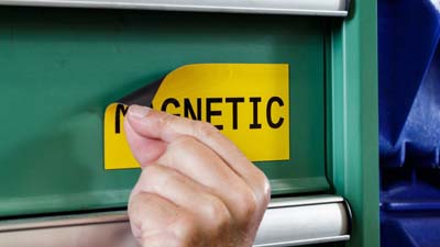 Bir ekipmanın metal kapağına manyetik olarak yapıştırılmış, Brady’nin manyetik polyester etiket malzemesinin, üzerine MAGNETIC yazısı basılmış bir örneği.