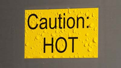 Üzerinde CAUTION HOT yazan sarı renkli Brady ToughWash etiket. Etiket, sanki yeni temizlenmiş gibi ıslak.